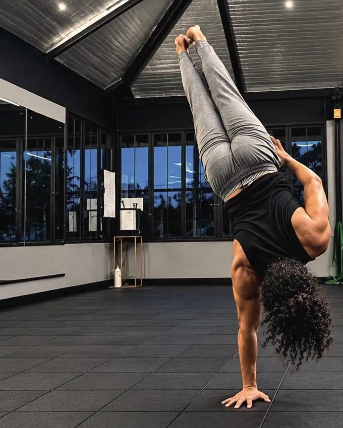 Nithin balancing in a one-arm handstand, legs together and pointed to the ceiling