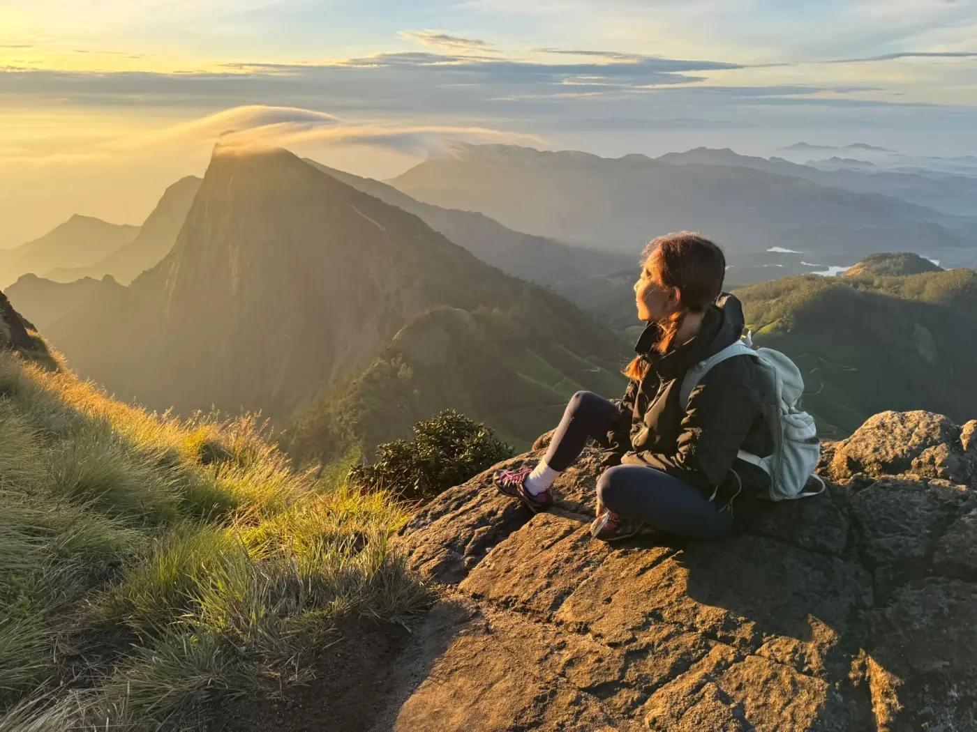 A retreat guest sits on a rock above the Western Ghats at sunrise, cloud pouring over a peak beyond