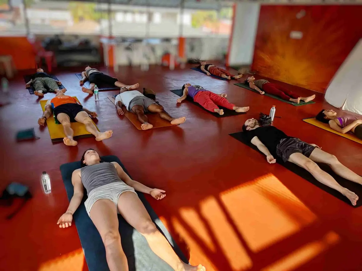 Students resting in savasana across the red floor of the studio while afternoon sunlight falls through the open walls